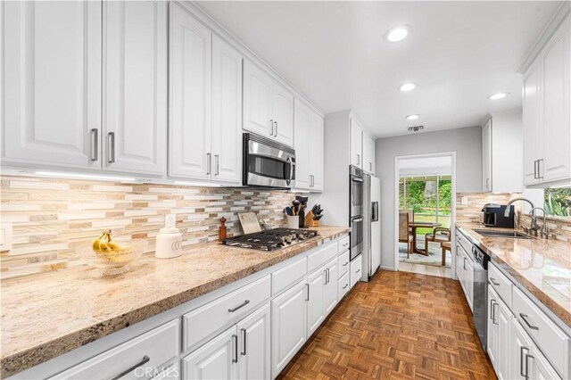 kitchen featuring appliances with stainless steel finishes, recessed lighting, white cabinets, a sink, and light stone counters