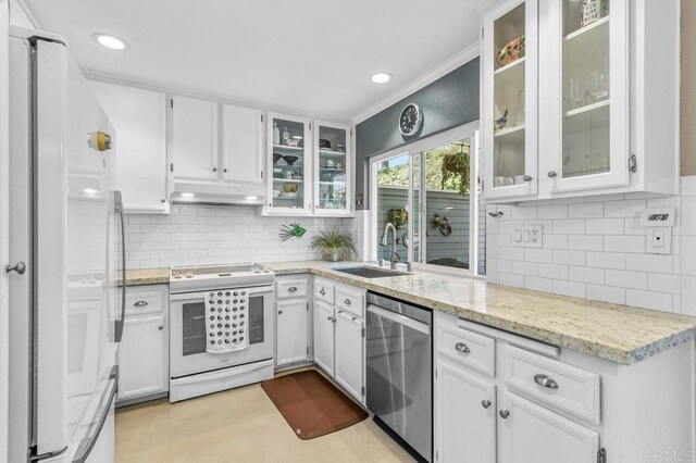 kitchen featuring white appliances, a sink, under cabinet range hood, tasteful backsplash, and white cabinets