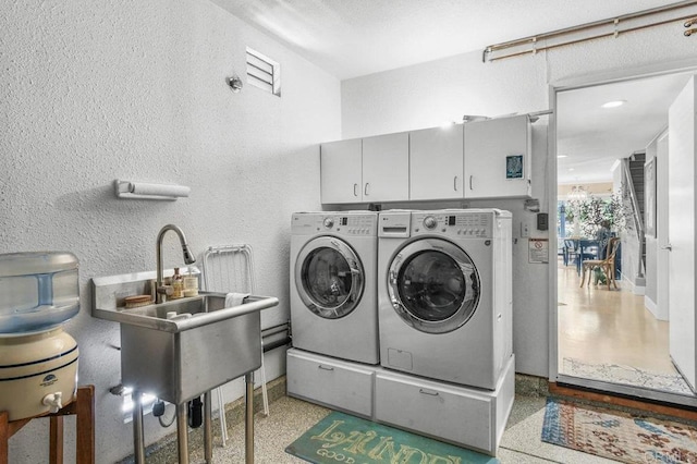 clothes washing area featuring separate washer and dryer, cabinet space, and a textured wall