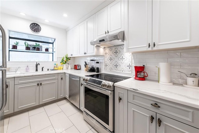 kitchen with under cabinet range hood, stainless steel appliances, a sink, light tile patterned floors, and gray cabinets
