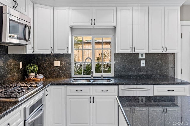 kitchen featuring appliances with stainless steel finishes, a sink, white cabinets, and tasteful backsplash