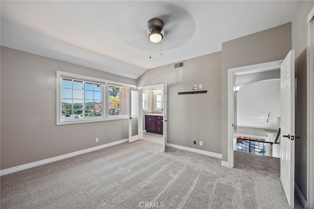 unfurnished bedroom with light carpet, baseboards, lofted ceiling, ensuite bathroom, and ceiling fan