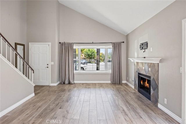 unfurnished living room with a premium fireplace, wood finished floors, baseboards, and high vaulted ceiling