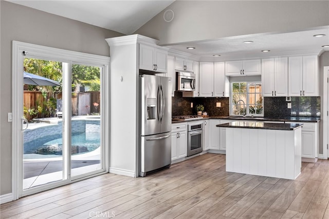 kitchen with appliances with stainless steel finishes, dark countertops, white cabinets, tasteful backsplash, and vaulted ceiling
