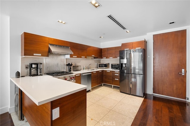 kitchen with stainless steel appliances, under cabinet range hood, a peninsula, a sink, and light countertops