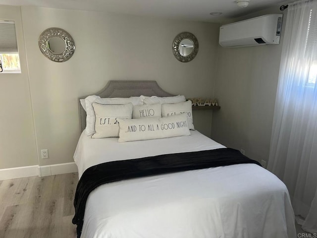 bedroom with wood finished floors, a wall unit AC, and baseboards