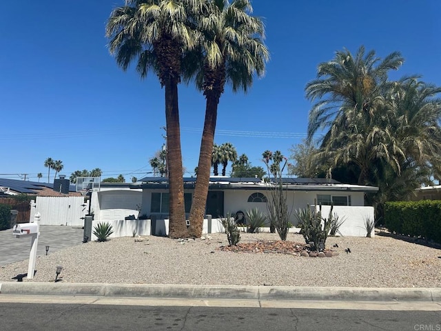 ranch-style home featuring driveway, roof mounted solar panels, a gate, stucco siding, and fence