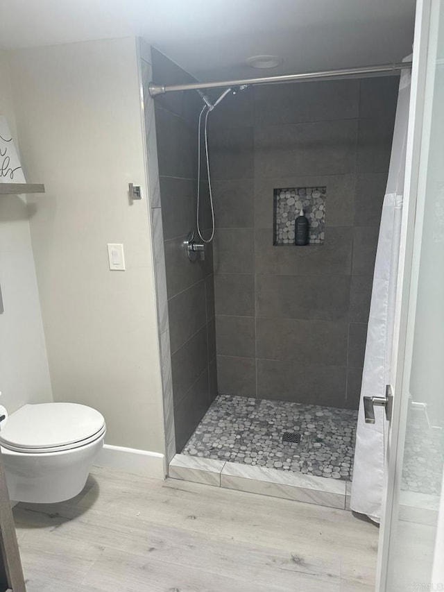 bathroom with wood finished floors, a shower stall, and toilet