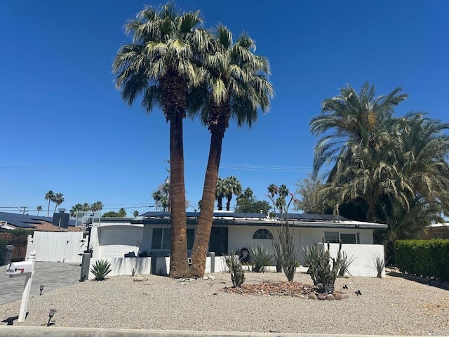 ranch-style home featuring driveway, an attached garage, a gate, roof mounted solar panels, and stucco siding
