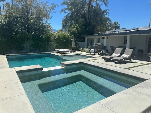 view of swimming pool featuring a patio area, a pool with connected hot tub, and a grill