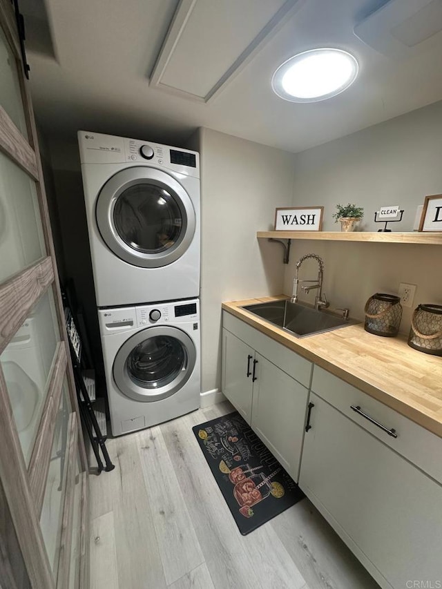 laundry area featuring stacked washing machine and dryer, light wood-type flooring, and cabinet space