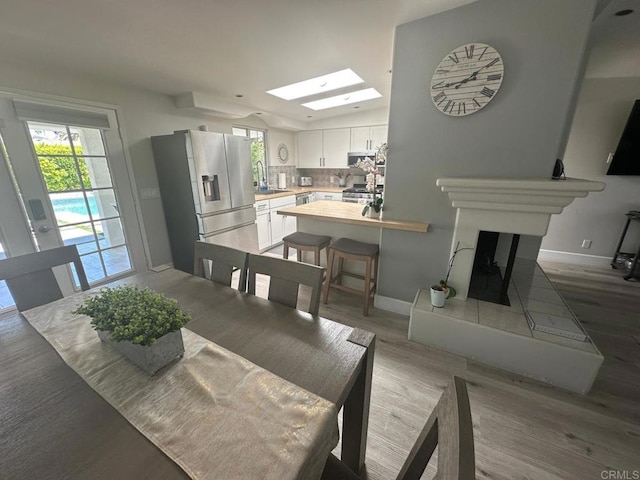 dining area featuring wood finished floors, baseboards, a fireplace with raised hearth, and a skylight