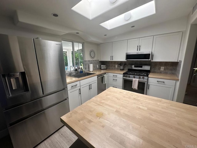 kitchen with appliances with stainless steel finishes, a sink, a skylight, wooden counters, and tasteful backsplash