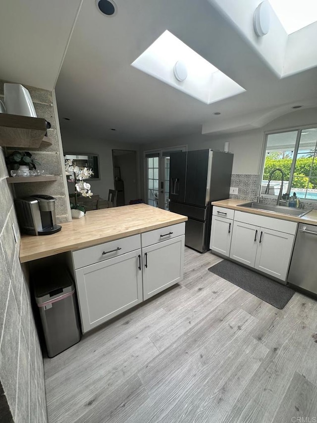 kitchen with a sink, a skylight, wooden counters, and freestanding refrigerator