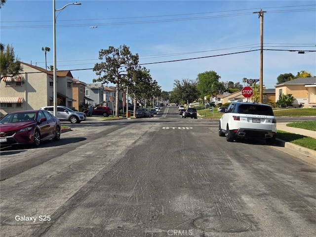 view of asphalt street featuring a residential view, street lights, sidewalks, curbs, and traffic signs