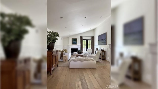 living room featuring a fireplace, a decorative wall, light wood-type flooring, vaulted ceiling, and a wainscoted wall