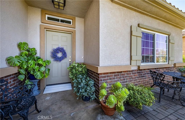 view of exterior entry with stucco siding and brick siding