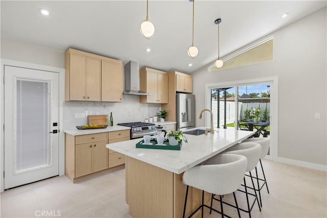 kitchen with light brown cabinets, a sink, wall chimney range hood, appliances with stainless steel finishes, and high vaulted ceiling