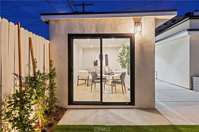 view of exterior entry with stucco siding, fence, and a patio