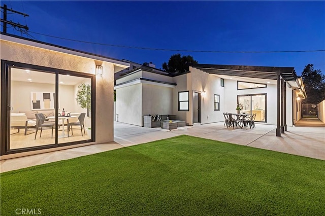 back of house at night featuring stucco siding, a patio area, and a yard