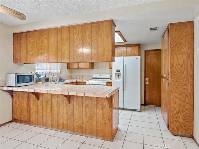 17949 Catalpa St, Hesperia, CA 92345 - kitchen featuring white appliances, a peninsula, tile counters, brown cabinets, and light tile patterned flooring