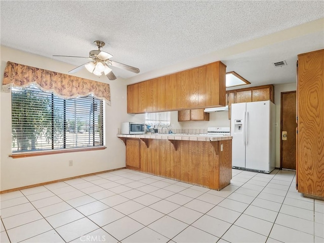 17949 Catalpa St, Hesperia, CA 92345 - kitchen featuring white fridge with ice dispenser, tile counters, a peninsula, brown cabinetry, and a kitchen bar