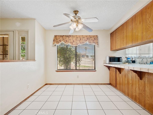 17949 Catalpa St, Hesperia, CA 92345 - kitchen with stainless steel microwave, tile countertops, brown cabinetry, a textured ceiling, and ceiling fan