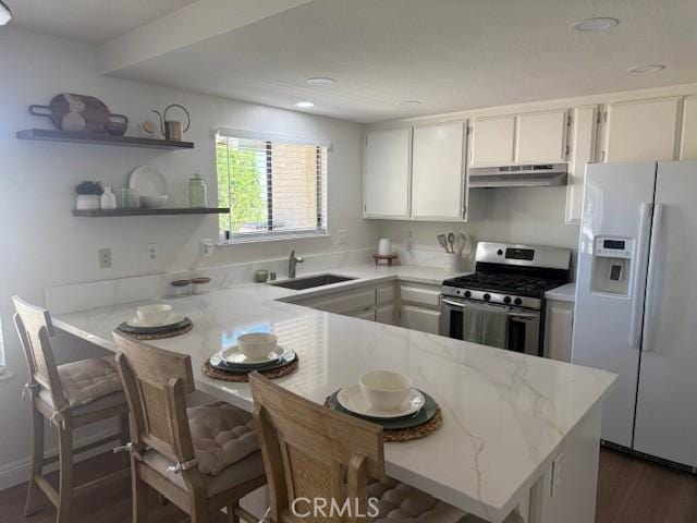 17949 Catalpa St, Hesperia, CA 92345 - kitchen featuring white refrigerator with ice dispenser, stainless steel gas stove, under cabinet range hood, a peninsula, and white cabinetry