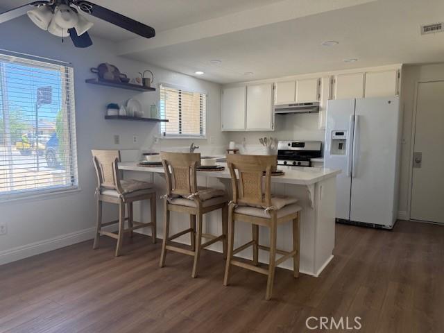 17949 Catalpa St, Hesperia, CA 92345 - kitchen with white refrigerator with ice dispenser, stainless steel stove, under cabinet range hood, dark wood finished floors, and a peninsula