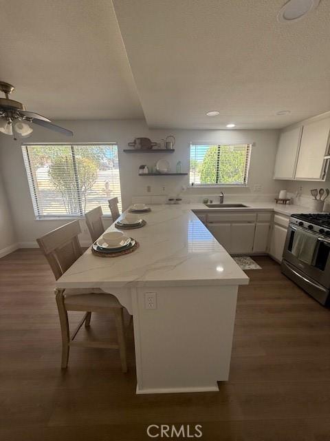 17949 Catalpa St, Hesperia, CA 92345 - kitchen with stainless steel range with gas stovetop, white cabinetry, dark wood-style flooring, a breakfast bar area, and ceiling fan