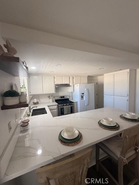 17949 Catalpa St, Hesperia, CA 92345 - kitchen featuring gas stove, white refrigerator with ice dispenser, a peninsula, under cabinet range hood, and light stone counters