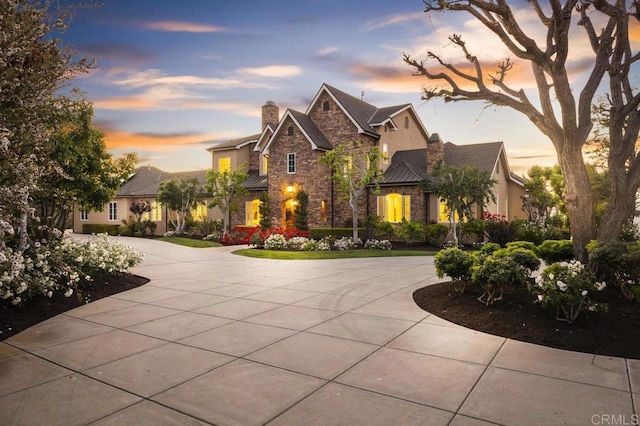 view of front of property featuring stone siding, curved driveway, a chimney, and stucco siding
