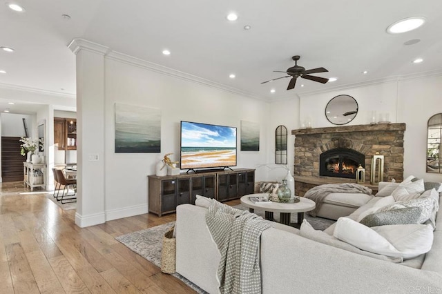 living room featuring a ceiling fan, crown molding, baseboards, light wood-type flooring, and a stone fireplace