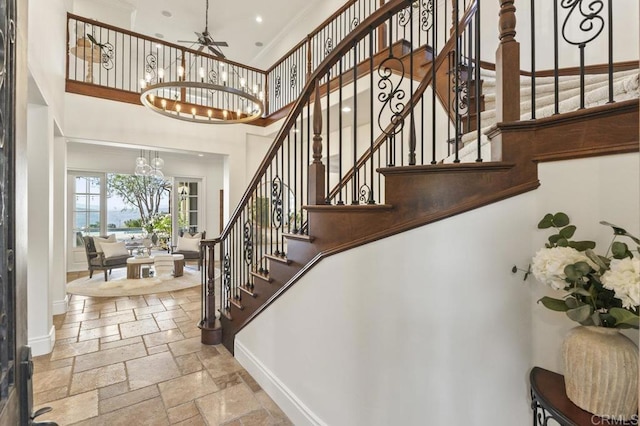 staircase featuring a chandelier, a towering ceiling, baseboards, stone tile flooring, and crown molding