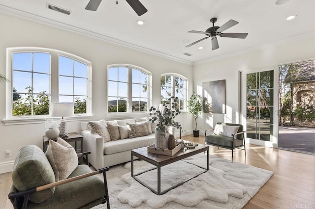 living area with ceiling fan, healthy amount of natural light, recessed lighting, ornamental molding, and wood finished floors