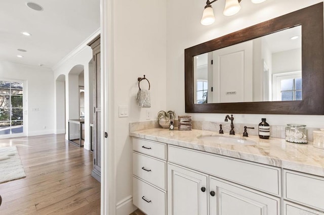 bathroom featuring ornamental molding, baseboards, wood finished floors, vanity, and recessed lighting
