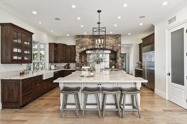 kitchen with built in refrigerator, a sink, a large island, dark brown cabinets, and recessed lighting