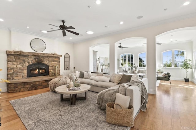 living room featuring arched walkways, ceiling fan, light wood finished floors, crown molding, and recessed lighting