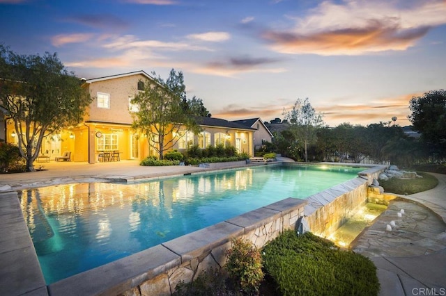 pool at dusk with an infinity pool and a patio area