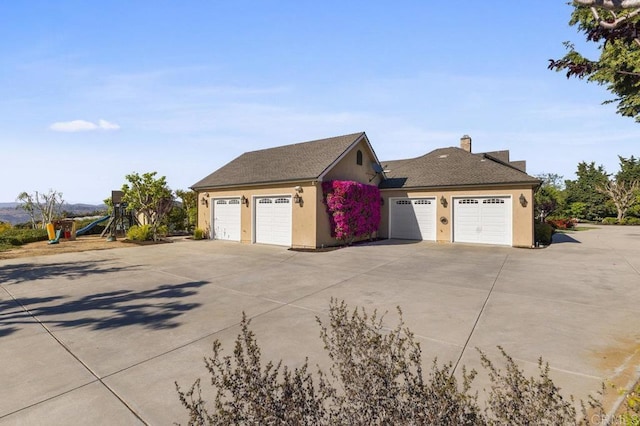 view of home's exterior featuring a garage, stucco siding, a chimney, and a playground