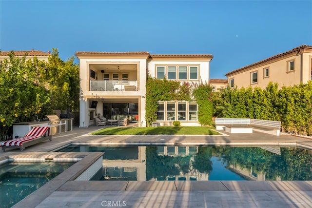 rear view of property with a balcony, a patio, stucco siding, an outdoor pool, and a tiled roof