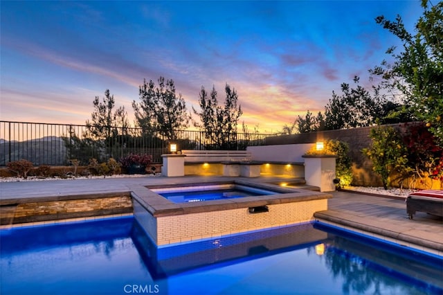 pool at dusk with an in-ground hot tub and fence