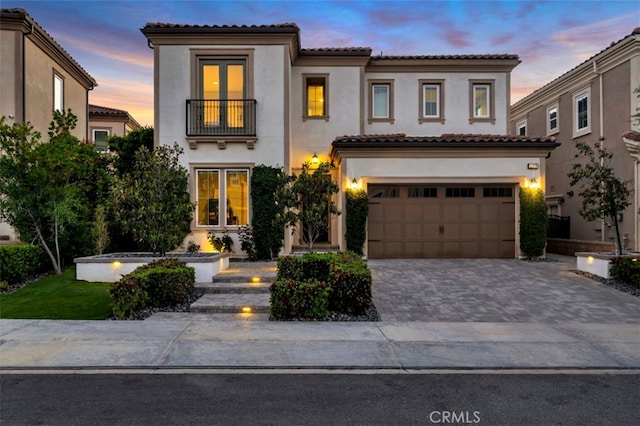 mediterranean / spanish-style home with a balcony, stucco siding, driveway, and an attached garage