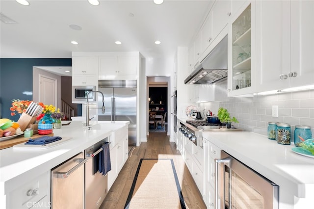 kitchen featuring under cabinet range hood, a sink, built in appliances, wine cooler, and light wood-style floors