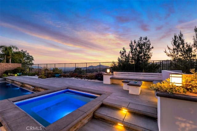 pool at dusk with an in-ground hot tub, fence, a patio, and an outdoor fire pit