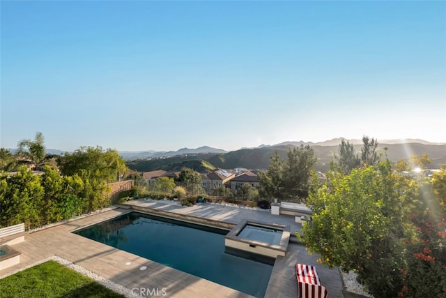 swimming pool with an in-ground hot tub, a mountain view, a fenced backyard, and a patio