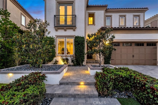 mediterranean / spanish-style house featuring a balcony, stucco siding, a garage, and driveway