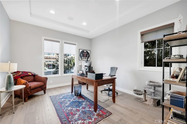 office space featuring plenty of natural light, light wood-style flooring, baseboards, recessed lighting, and a raised ceiling