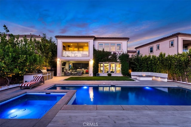 back of house featuring an in-ground hot tub, a balcony, a patio area, an outdoor pool, and a tiled roof