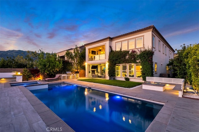 rear view of house with a balcony, a patio, stucco siding, a tile roof, and a pool with connected hot tub